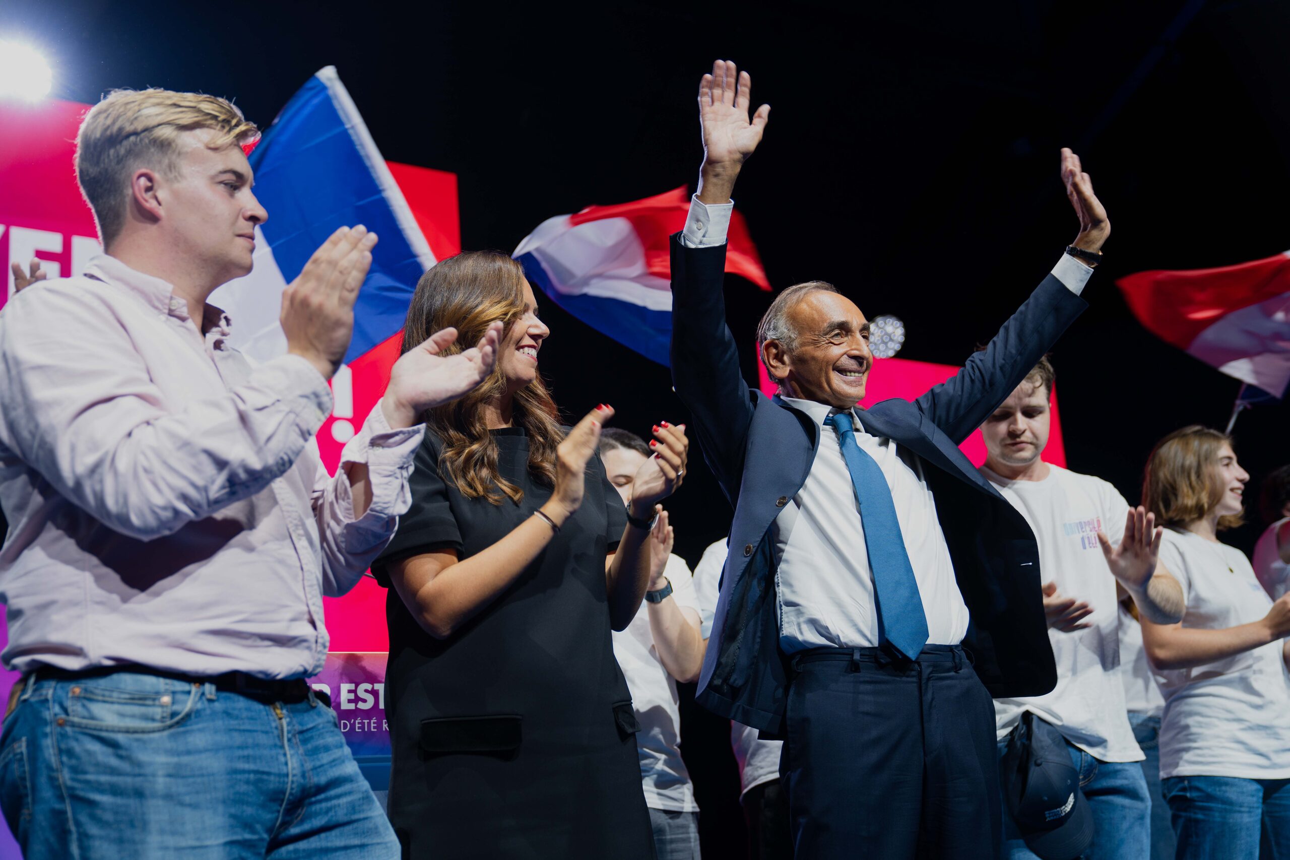 Éric Zemmour et Sarah Knafo saluent le public sur scène avec de jeunes militants, à l’université d’été 2026 de Reconquête